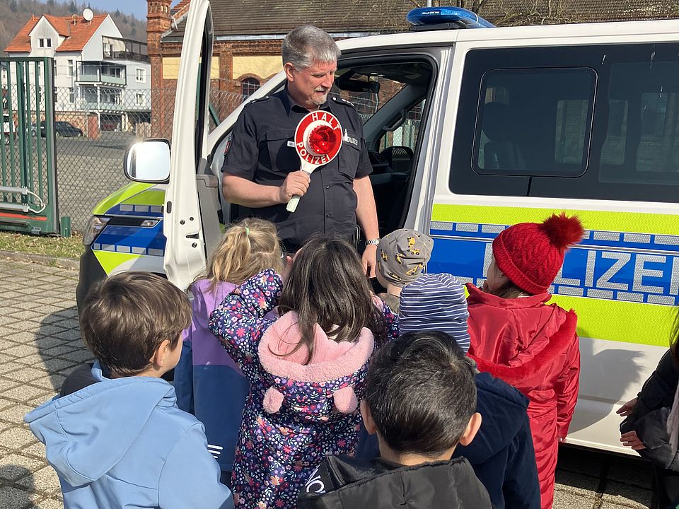 Polizist vor Polizeiauto mit einer Gruppe Kindern der DRK-Kita Scheden bei ihrem Besuch in der Polizeischule
