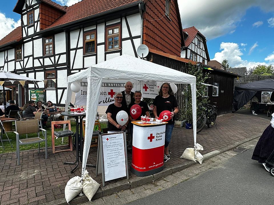 2026_09_15_Dorffest_Stand_Mitgliedergewinnung_OV_Landwehrhagen__2_.jpg Mitglieder des DRK-Ortsvereins Landwehrhagen im DRK-Kreisverband Göttingen-Northeim e. V. an einem DRK-Stand mit Luftballons und Pavillion
