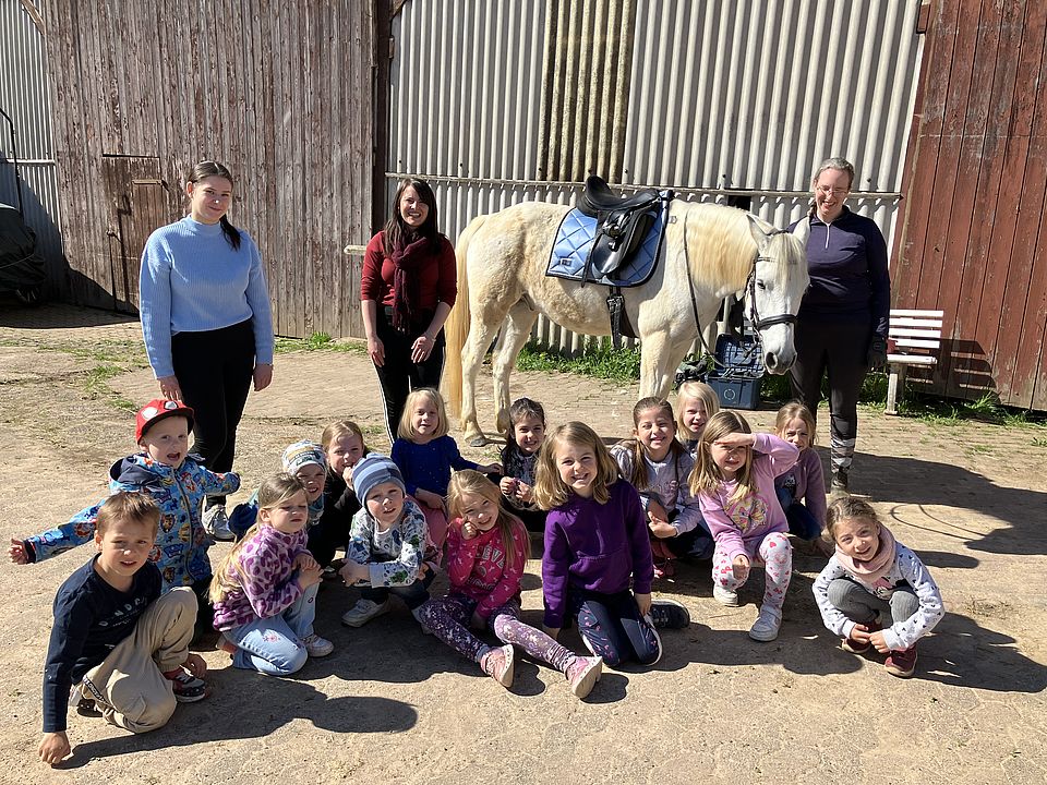 Reitstallausflug der DRK-Kita Scheden: Gruppenbild der Kinder und Erzieher*innen mit einem weißen Pferd
