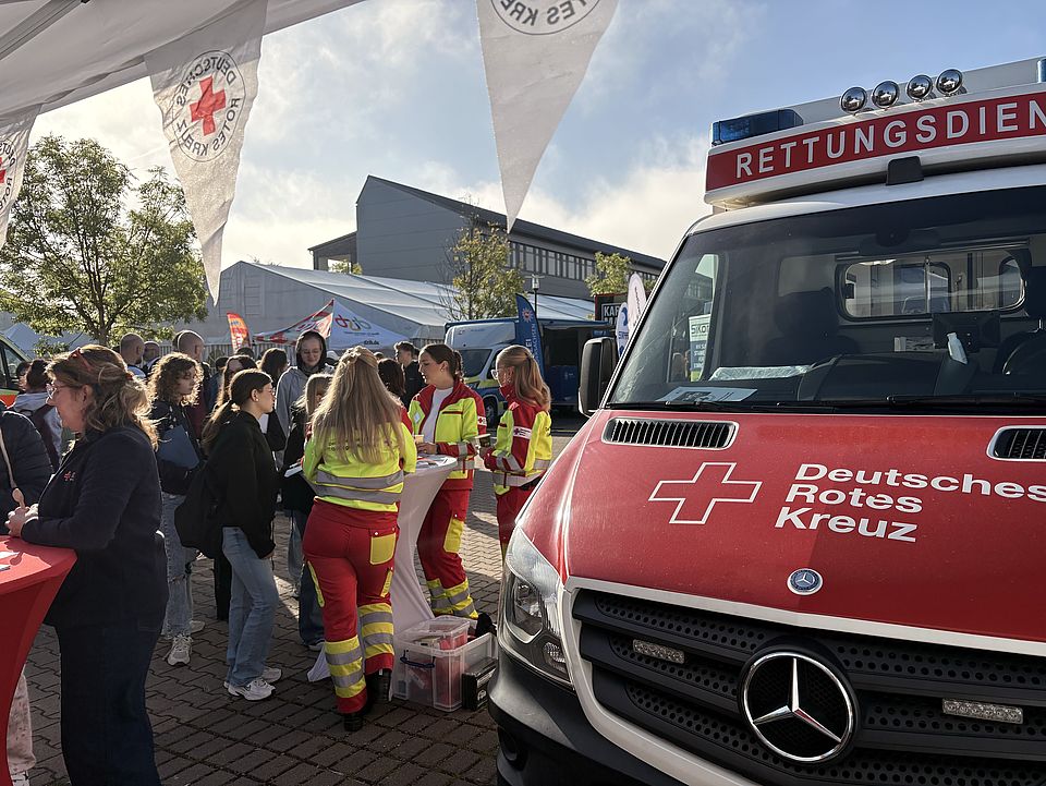 DRK-Stand auf der Einbecker Ausbildungsmesse mit Rettungswagen und vielen Menschen am Stand, Wimpelkette schmückt den Pavillion