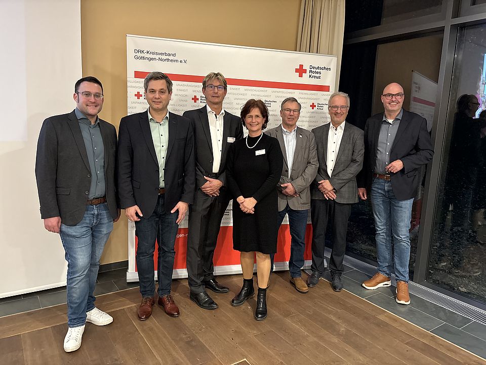 Kreisversammlung Gruppenfoto Gäste Frau Reußner als Vorstandsvorsitzende steht gemeinsam mit dem Präsidenten Herrn Prof. Dr. Hufenbach mit Teilnehmenden Gästen aus der Politik und der Öffentlichkeit vor der DRK-Pressewand