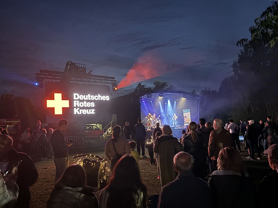 2026_09_26_Lichterlauf_am_Kiessee__20_.jpg DRK-Bereitschaft Göttingen beim Sanitätsdienst am Göttinger Kiessee beim Lichterlauf, Bühne mit Menschen davor und Bildschirm mit Logo des DRK daneben