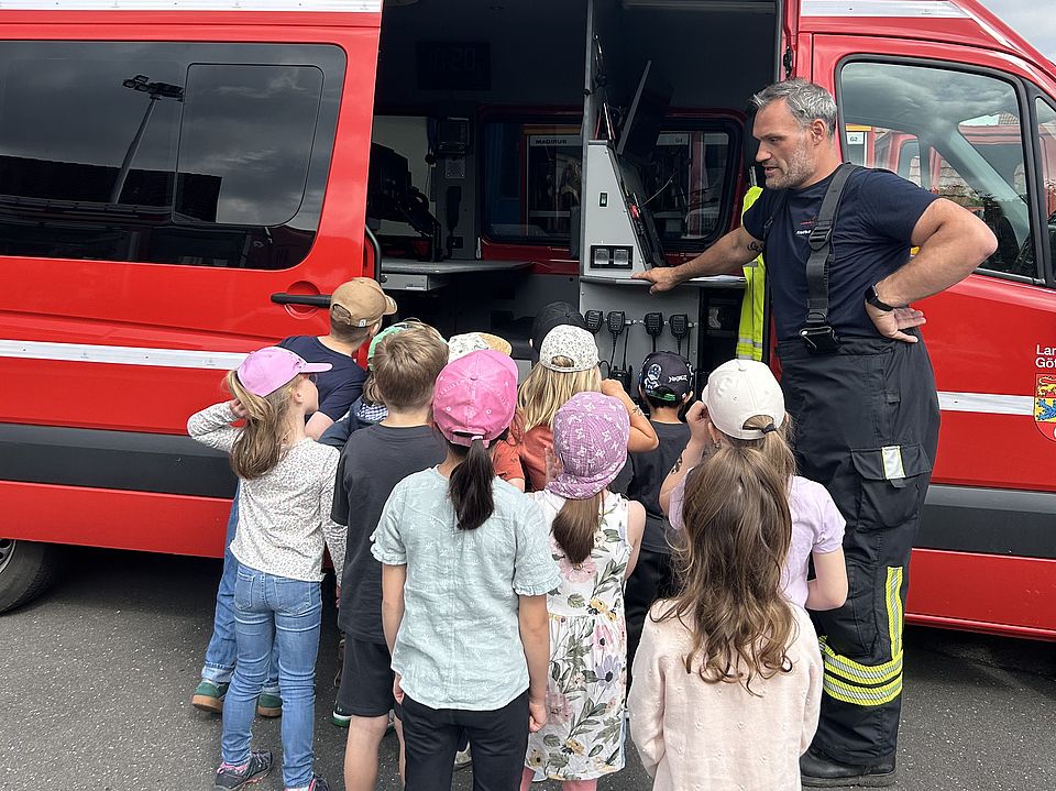 Kinder der DRK-Kita Volkmarshausen schauen in einen geöffneten Rettungswagen, während eine Einsatzkraft der Feuerwehr Gimte das Innenleben erklärt.