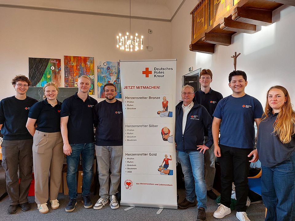 2026_09_21_Ehrenamtliches_DRK-Team_und_Markus_Schiffer__Woche_der_Wiederbelebung.jpg Gruppenfoto des ehrenamtlichen DRK-Teams für Erste-Hilfe-Ausbildung vor einem Informationsbanner zur Herz-Lungen-Wiederbelebung. Die Aufnahme entstand im Rahmen der Woche der Wiederbelebung an der Bonifatiusschule und zeigt die beteiligten Ausbilder*innen sowie Fachbereichsleiter Markus Schiffer gemeinsam im Veranstaltungsraum