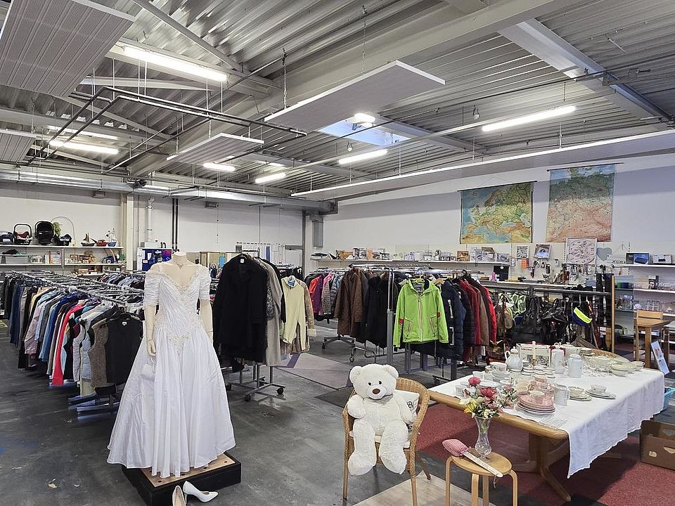 2026_01_28_Aktion_Schüsseln_und_Schalen_für_1_Euro__4_.jpeg Man sieht das Göttinger Spendenzentrum des DRK von innen, mit vielen Ständern mit Kleidung und Tischen mit Gegenständen. Im Vordergrund sitzt ein weißer Teddybär und man sieht ein Hochzeitskleid an einem Mannequin