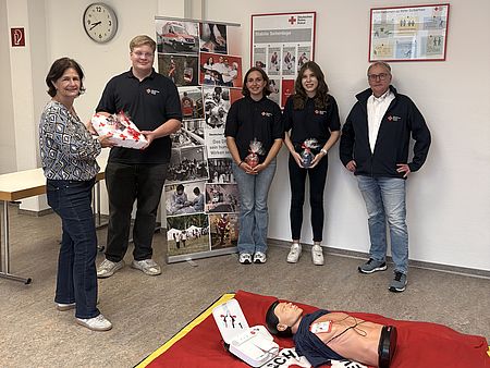 Verabschiedung und Begrüßung im DRK-Kreisverband Göttingen-Northeim e. V.: DRK-Kreisgeschäftsführerin und Erste-Hilfe Bereichsleiter zusammen mit den alten und neuen FSJlern in Bereich Erste-Hilfe halten Geschenke in den Händen, im Vordergrund eine Übungspuppe