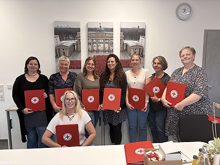 Gruppenaufnahme der Mitarbeitenden der Kita Löwenhagen und der DRK-Kita-Fachberatung bei einem Teamtag zur Übernahme der Trägerschaft durch den DRK-Kreisverband Göttingen-Northeim. Die Teilnehmenden stehen und sitzen in einem Besprechungsraum und halten rote DRK-Mappen in den Händen.