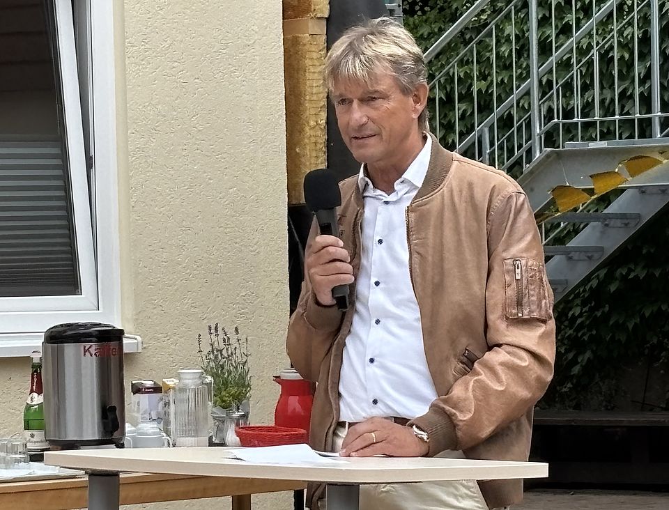 2026_07_04_Bundesverdienstkreuz_Jan_Störmer__2_.jpeg Rede von Präsident des DRK-Kreisverbandes Göttingen-Northeim e. V. Dr. Hufenbach mit Mikrofon bei Verleihung des Bundesverdienstkreuzes für DRK-Ehrenamt von Jan Störmer im DRK-Kreisverband Göttingen-Northeim e. V. im Haus des Jugendrotkreuzes Einbeck