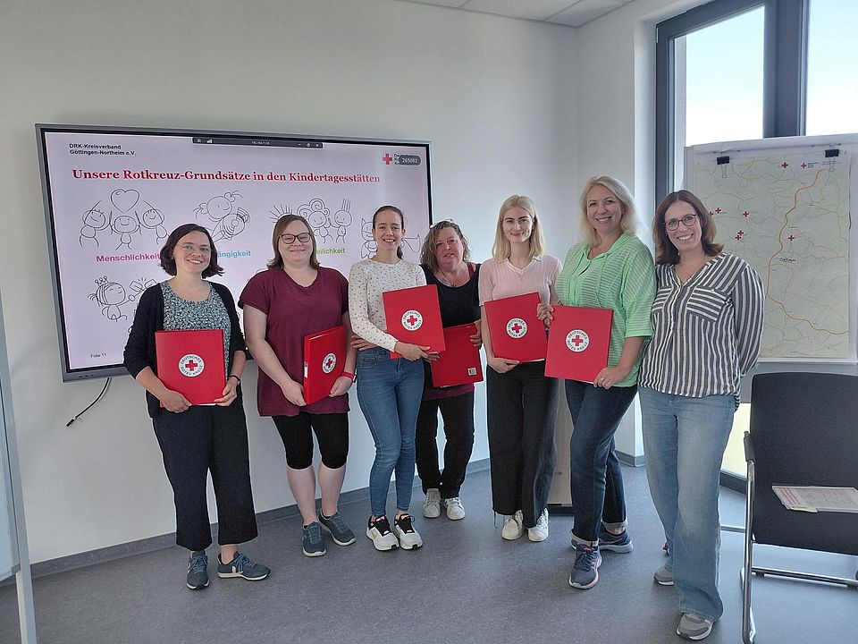 2026_09_14_Willkommenstag_Kita.jpg Neue Mitarbeitende in DRK-Kitas mit roten DRK-Mappen stehen vor einem Bildschirm mit einer Präsentation vom Roten Kreuz, gemeinsam mit DRK-Kreisverbands-Personalleitung Marion Laudenbach