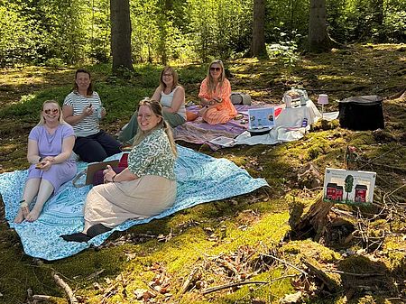 Team der Kita Bühren beim Outdoor-Teamtag des DRK-Kreisverbandes Göttingen-Northeim e. V. sitzt auf Decken im Wald.