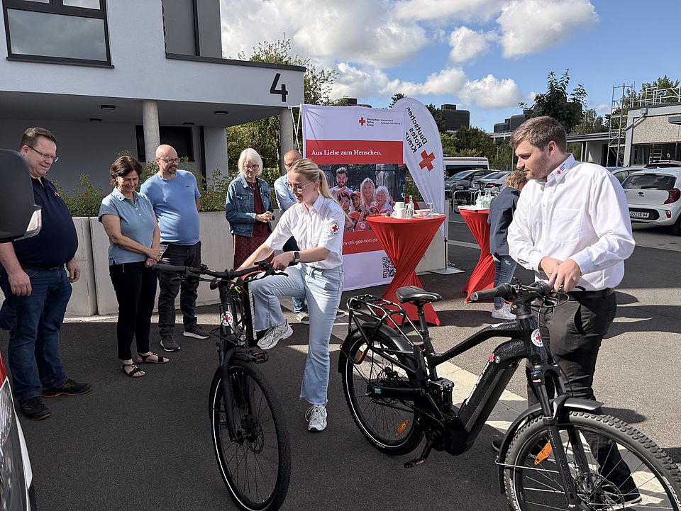2026_08_07_F3_Fahrradstaffel_Gründung_Aufnahmen_von_Miriam__13_.jpg Zwei Ehrenamtliche der Göttinger Bereitschaft, Mika Wolfram und Michelle Jonson,probieren die neuen E-Bikes der Fahrradstaffel aus, während weitere Gäste die Übergabe begleiten. Die Veranstaltung markiert die Gründung der ersten Fahrradstaffel des DRK-Kreisverbands Göttingen-Northeim für Sanitätsdienst und Katastrophenschutz