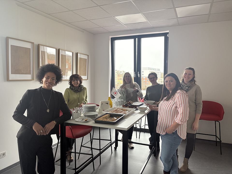 2026_03_17_Abschied_von_Stina__26_.jpg Mitarbeiterinnen des DRK-Kreisverbandes Göttingen-Northeim in der Küche ders Verwaltungsgebäudes, um einen Stehtisch herumstehend, bei der Verabschiedung von Stina Brüchmann als Vorstandsassistenz