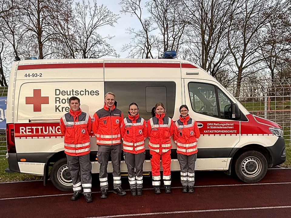 Ein Einsatzfahrzeug der DRK-Bereitschaft, davor stehen fünf Mitglieder der Bereitschaft in Uniform nebeneinander und schauen in die Kamera